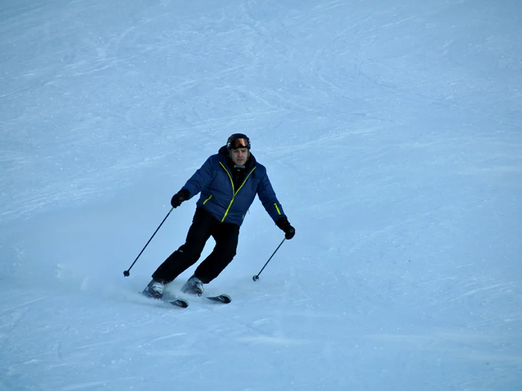 Skifahrer fährt mit angelegten Stöcken talwärts.
